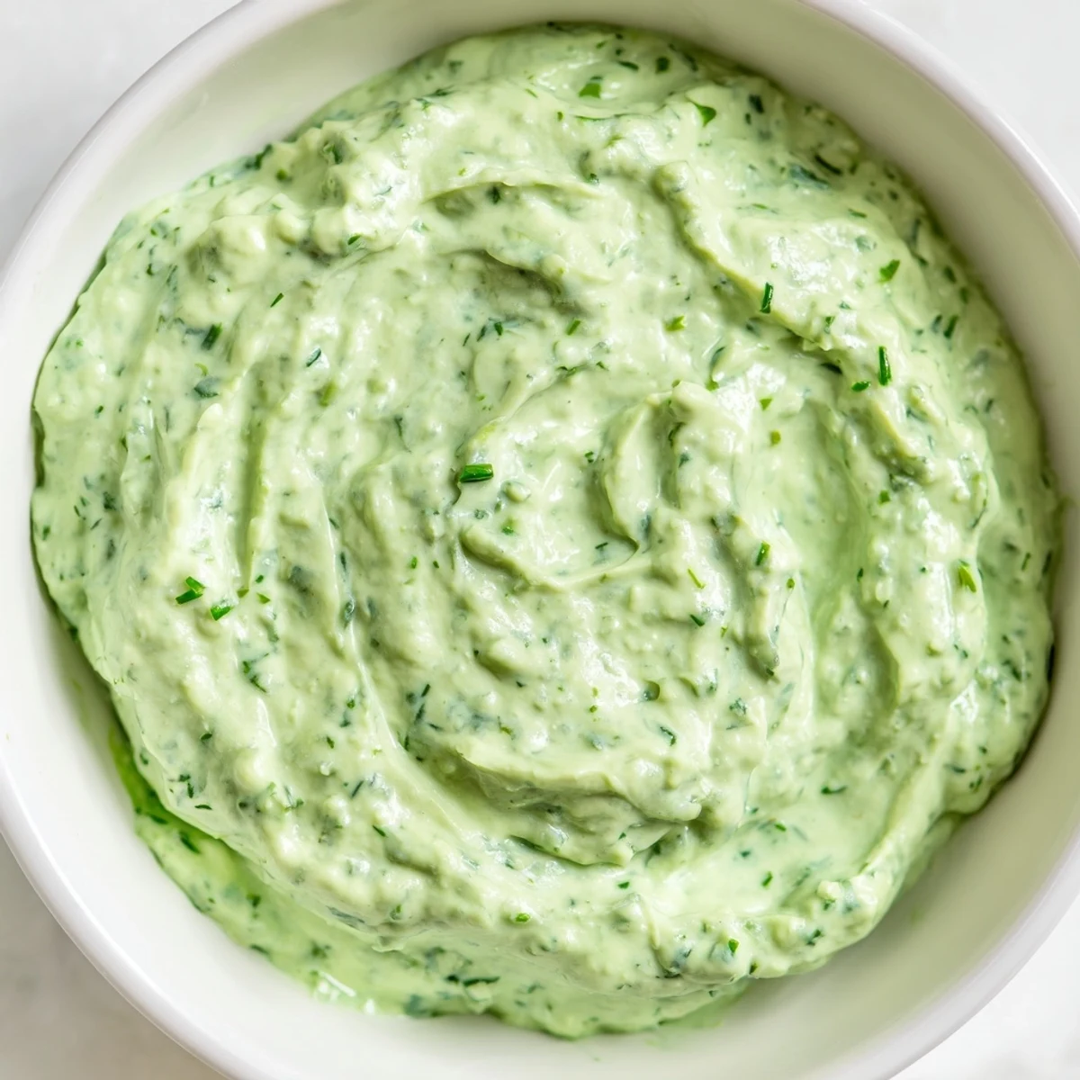A bowl of bright green Green Goddess Dip, ready to serve with colorful vegetables and crackers.