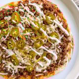 A sizzling Ground Beef Taco Pizza with a golden crust and a creamy sour cream drizzle.