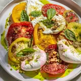 A beautiful heirloom tomato salad board, ready to serve with creamy burrata cheese and crusty bread.