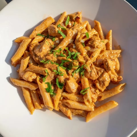 Golden penne pasta coated in creamy sauce of chicken tikka masala, garnished with fresh cilantro.