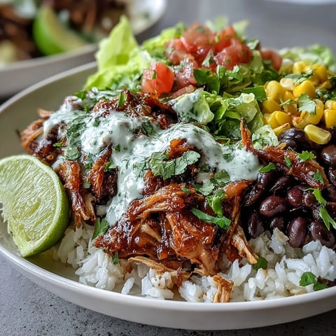 Golden-brown shredded carnitas sit atop fluffy rice, black beans, and crisp lettuce in a Carnitas Burrito Bowl, finished with a drizzle of lime crema.