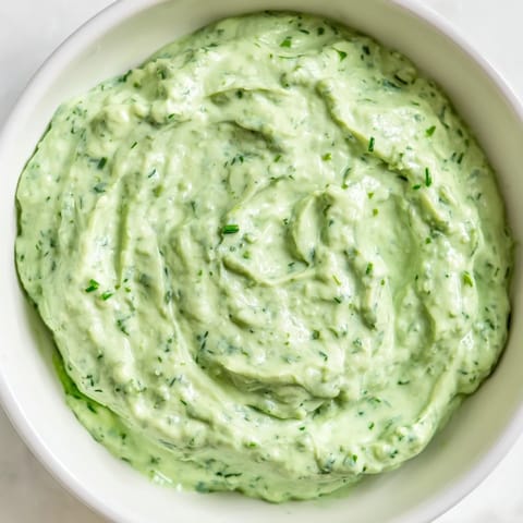 A bowl of bright green Green Goddess Dip, ready to serve with colorful vegetables and crackers.