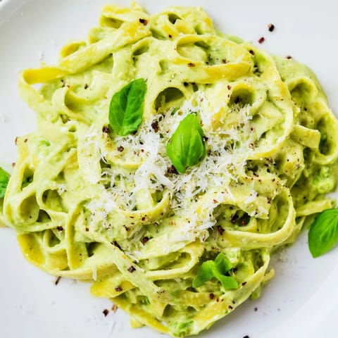 A skillet of creamy green pea Alfredo garnished with grated Parmesan and cracked black pepper, ready to serve.  