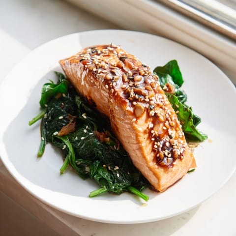 Miso salmon on sautéed spinach served on a white plate, garnished with lemon wedges and ready to enjoy.