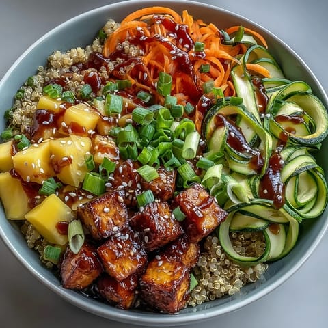 Colorful spiralized carrots and zucchini noodles crown a bowl of fluffy quinoa and crispy tofu, drizzled with sweet teriyaki sauce.