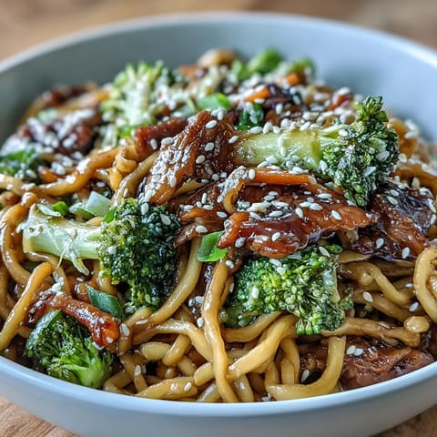 A close-up of a steaming Asian Teriyaki Noodle Bowl garnished with green onions and sesame seeds.