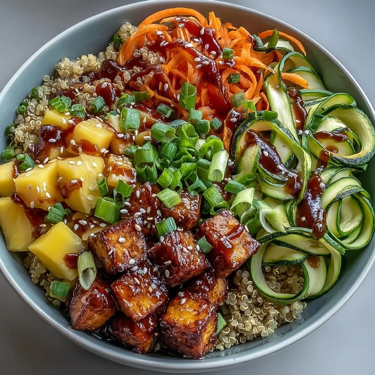 Colorful spiralized carrots and zucchini noodles crown a bowl of fluffy quinoa and crispy tofu, drizzled with sweet teriyaki sauce.