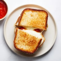 Golden-brown sourdough slices encase melted mozzarella cheese and crispy mozzarella sticks, creating a decadent grilled cheese sandwich perfect for dipping in warm marinara.  