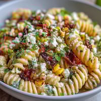 Vibrant elote corn pasta salad with charred sweet corn, creamy lime dressing, and crumbled Cotija cheese for a Mexican-inspired dish.